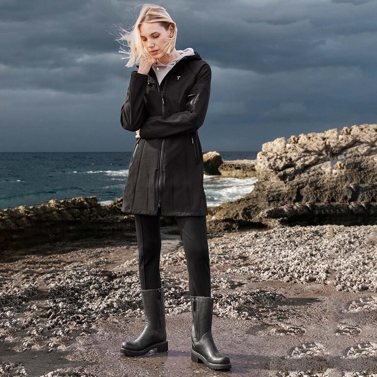 Frau in Ilse Jacobsen Softshell-Regenmantel bei windigem Wetter am Meer.