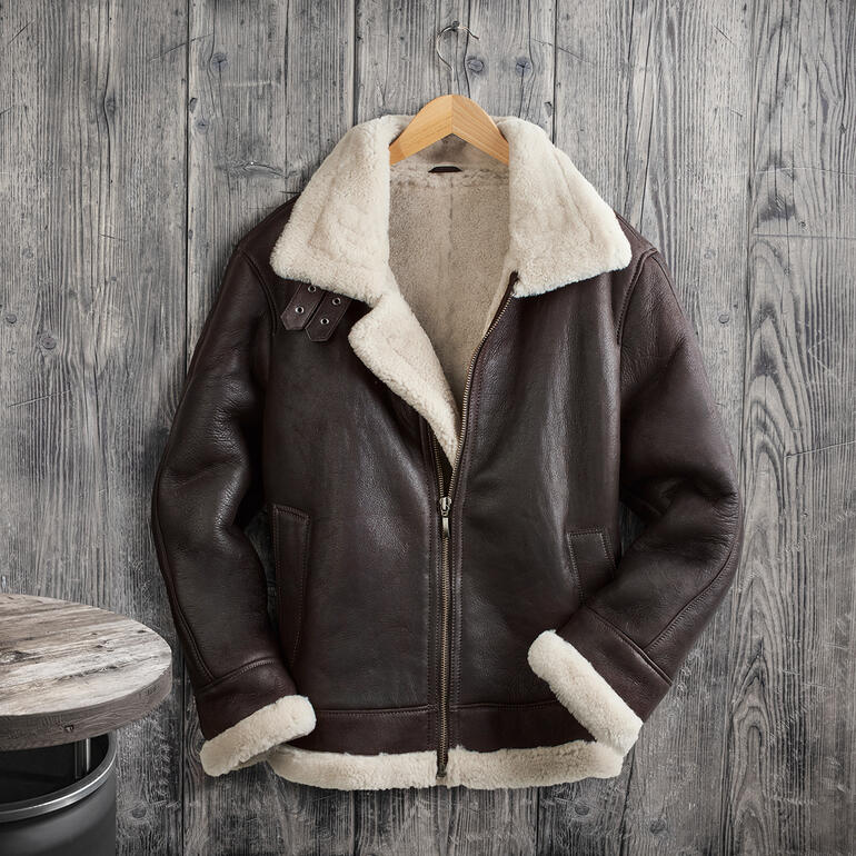 Lammfell-Fliegerjacke B3 auf Holzoberfläche aufgehängt.