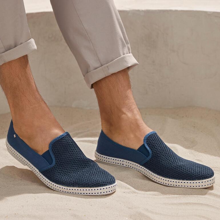 Mann mit Rivieras Sommer-Slipper in Dunkelblau, steht auf sandigem Boden.