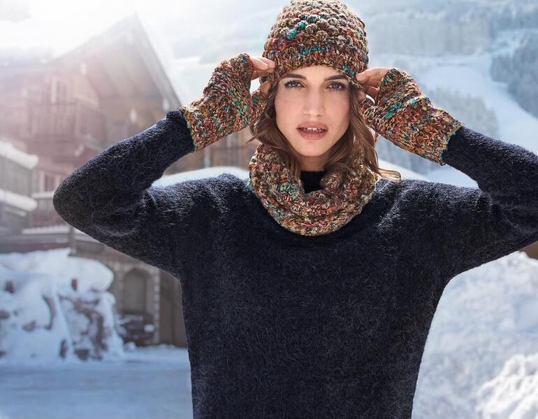 Frau mit bunter Mütze und Handschuhen in schneebedeckter Landschaft.