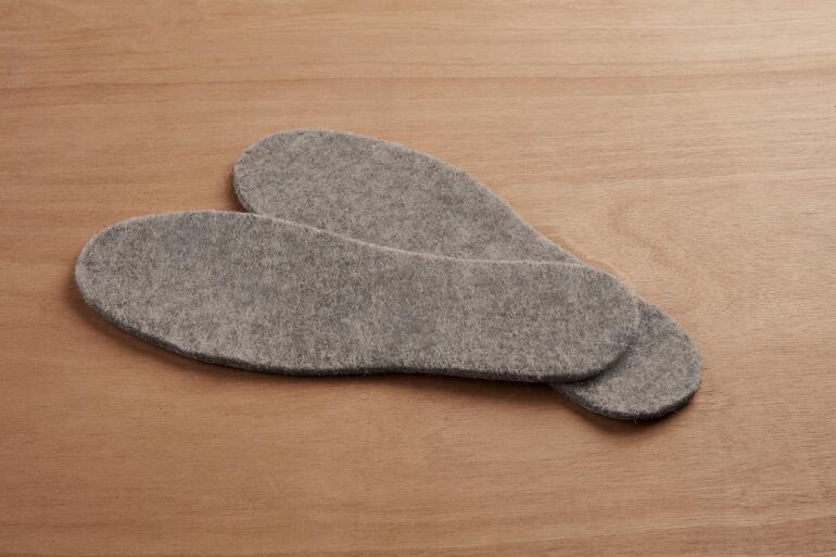 Zwei graue Alpakathermo-Schuheinlagen auf Holzuntergrund.