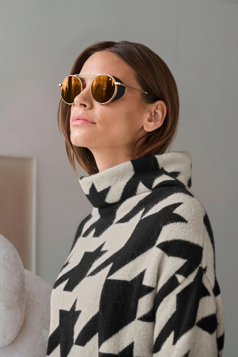 Frau mit Sonnenbrille in gold, trägt einen Pullover mit Sternen-Muster.