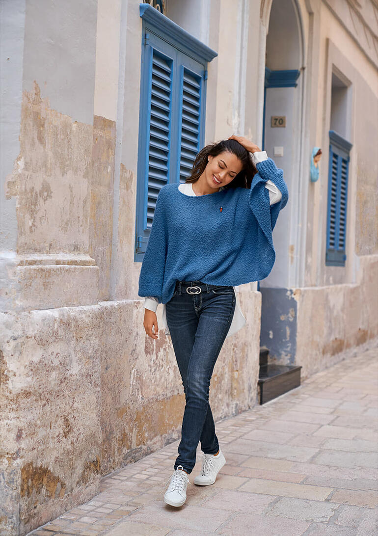 Frau trägt blauen Bouclé-Poncho-Pullover in einer Altstadtgasse