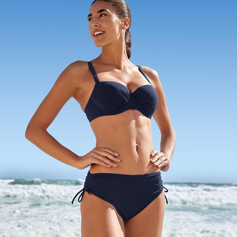 Dunkelblauer Sunflair® ReNew-Bikini getragen von einer Frau am Strand.