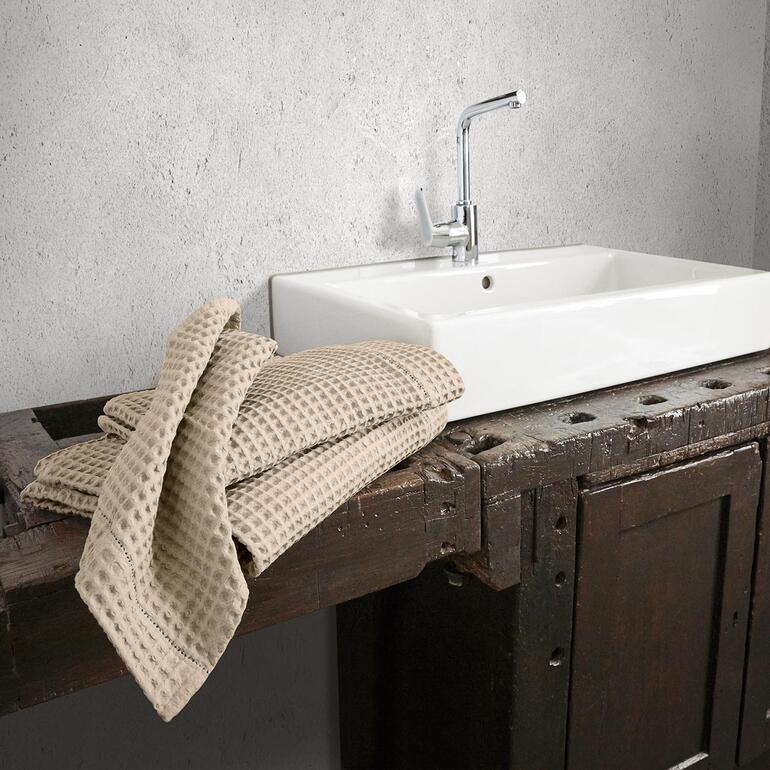 Beige Waffelpiqué-Handtücher, die über eine Holzoberfläche liegen.