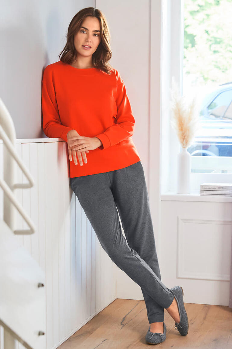 Frau in rotem Sweatshirt und grauen Jogginghosen lehnt an einer Treppe.