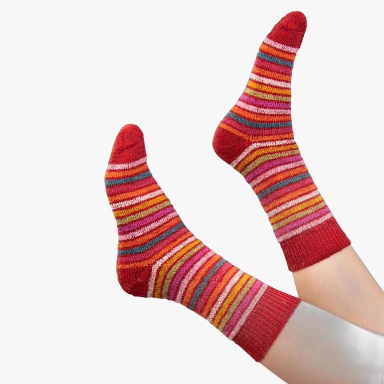 Paar rote Regenbogen-Ringelsocken an den Füßen.