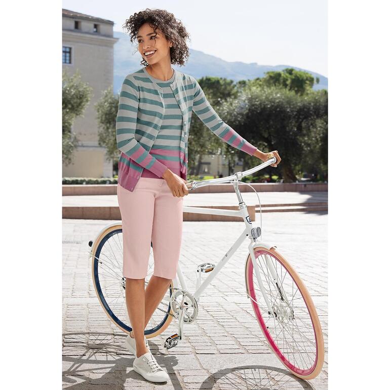 Frau in einem gestreiften Oberteil und rosa Hose steht neben einem Fahrrad.