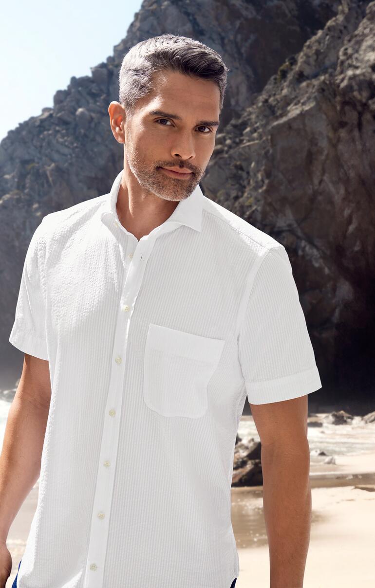 Mann in weißem Seersucker-Hemd im Freien, mit Felsen im Hintergrund.