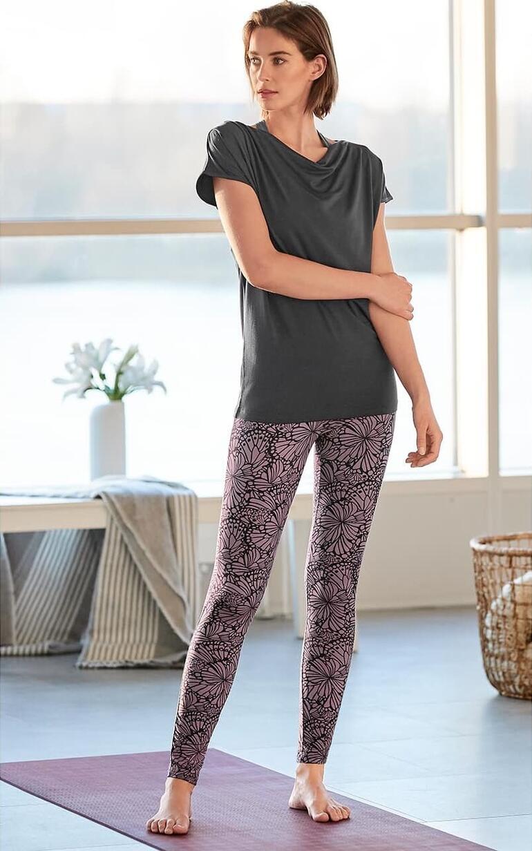 Frau in Yoga-Wasserfall-Shirt und floralem Leggings, stehend auf einer Yogamatte
