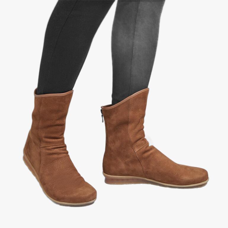 Braune arche Stierleder-Stiefelette, lässig am Fuß einer Person, die schwarze Leggings trägt.