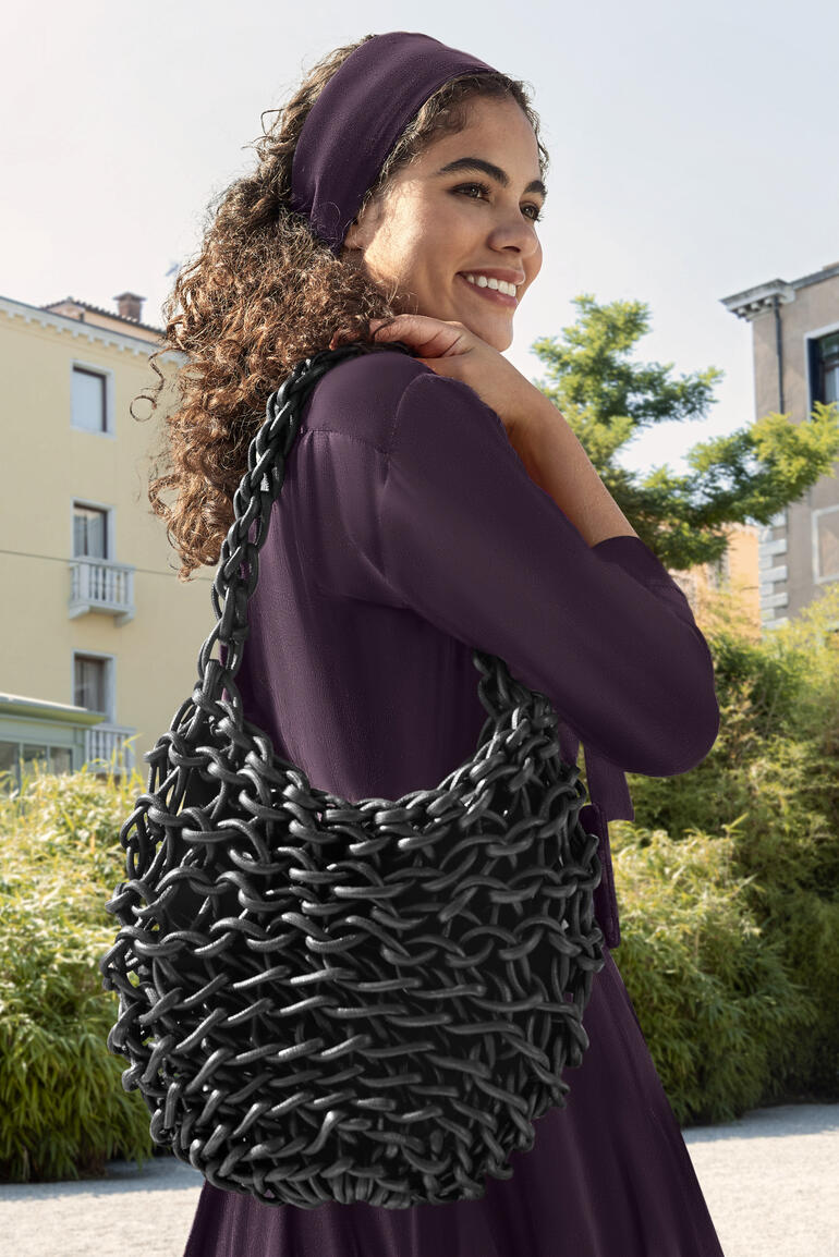 Glänzende schwarze Flechtasche Alienina, von einer Frau getragen.