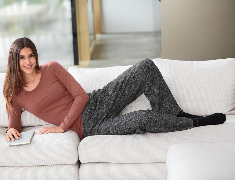 Frau in Braunem Alpaka-Pima-Shirt und grauen Hosen, entspannt auf Sofa.