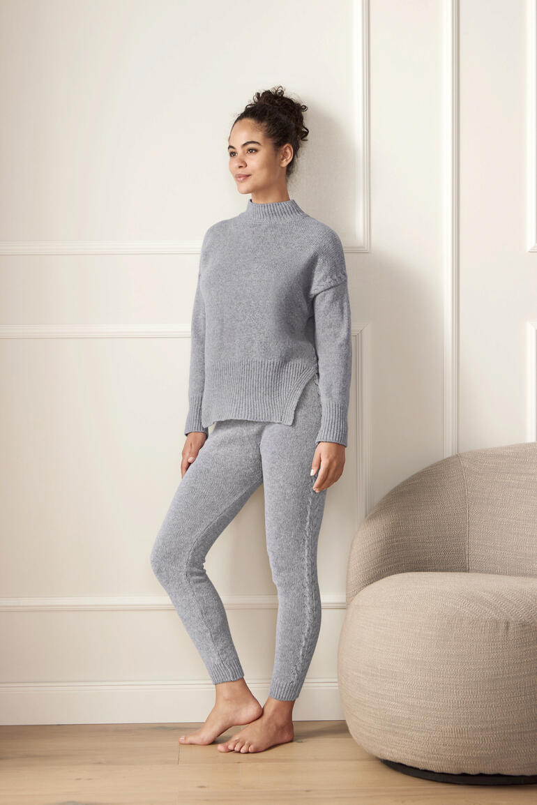 Frau trägt grauen Merino-Pullover und Leggings in einem hellen Raum