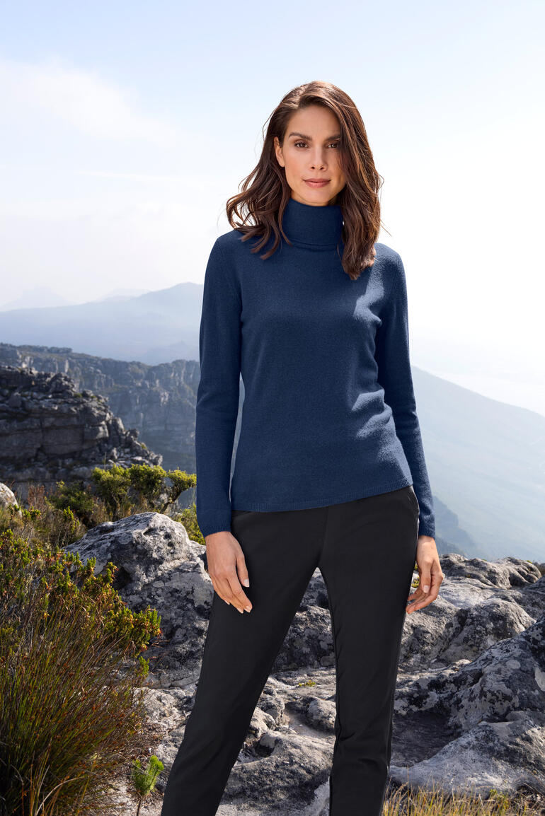 Frau in navy Kaschmir Rolli steht in der Natur, eindrucksvoller Berg Hintergrund.