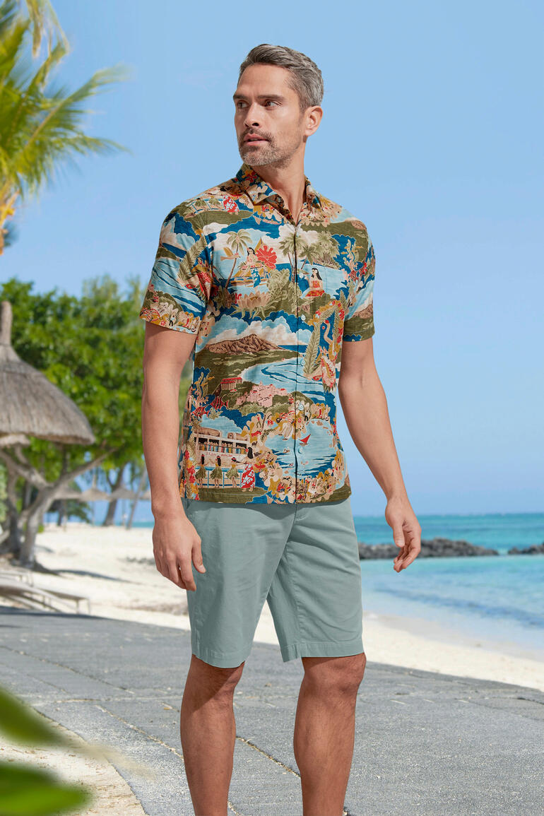 Salbei Mann in einem bunten Aloha-Shirt steht am Strand, umgeben von Palmen.
