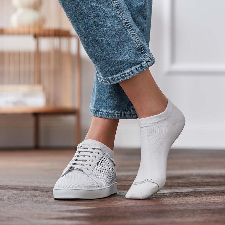 Füße in Sneakers mit einer weißen Sneakersocke, die auf einem Fuß sichtbar ist.