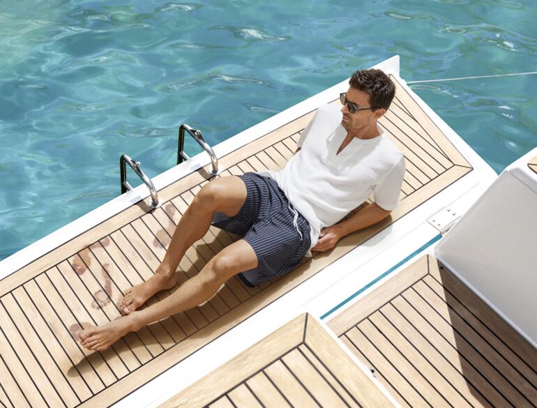 Mann in weißen Shorts sitzt am Steg neben einem Pool.