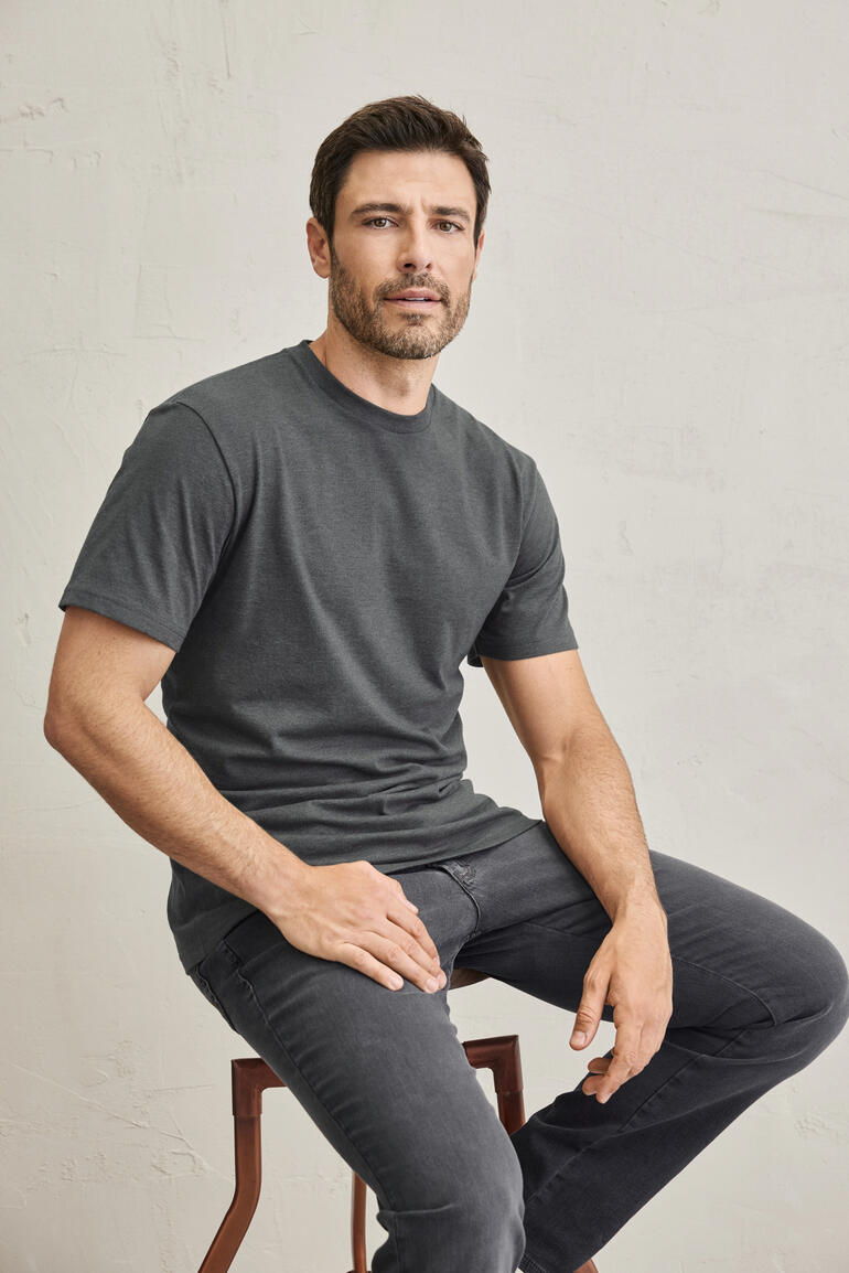 Mann sitzt mit grauem Ragman T-Shirt auf einem Stuhl