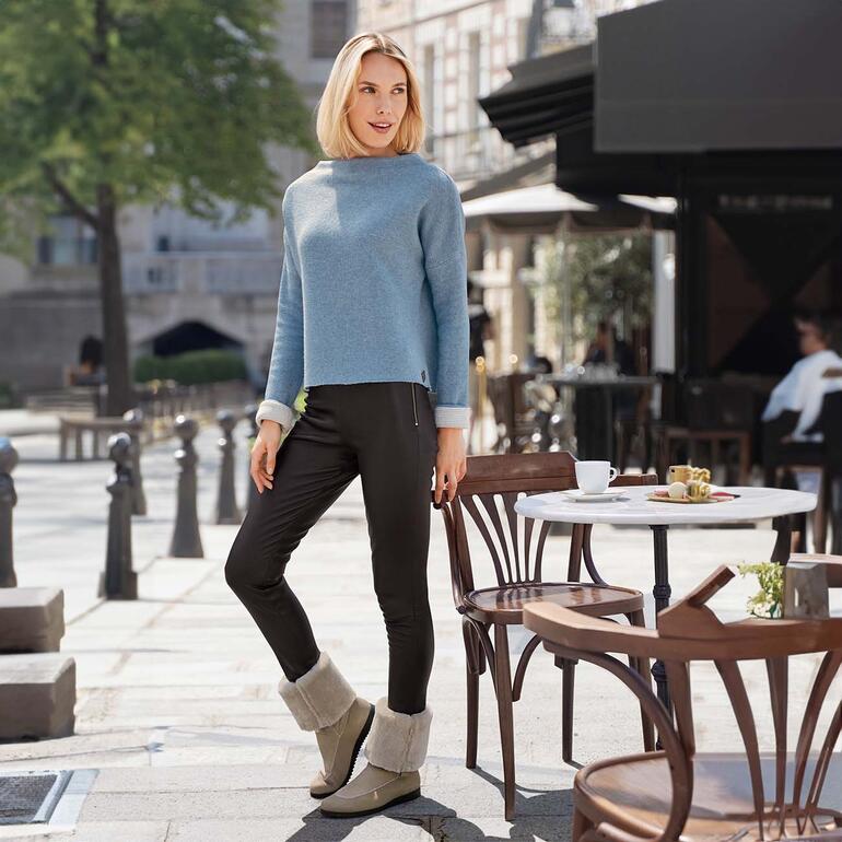 Frau in hellblauem Pullover und Lammfellboots sitzt im Freien.
