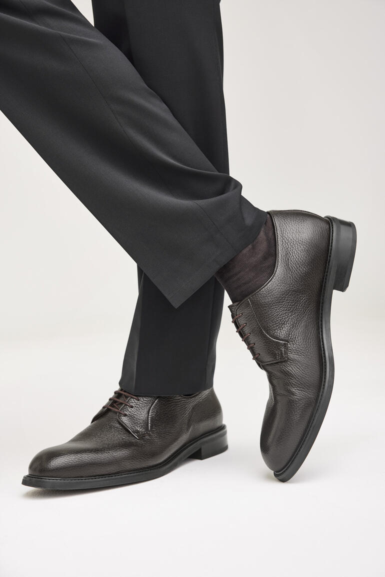 Mann trägt braune Hirschleder-Business-Schuhe, halb sitzt im Anzug.