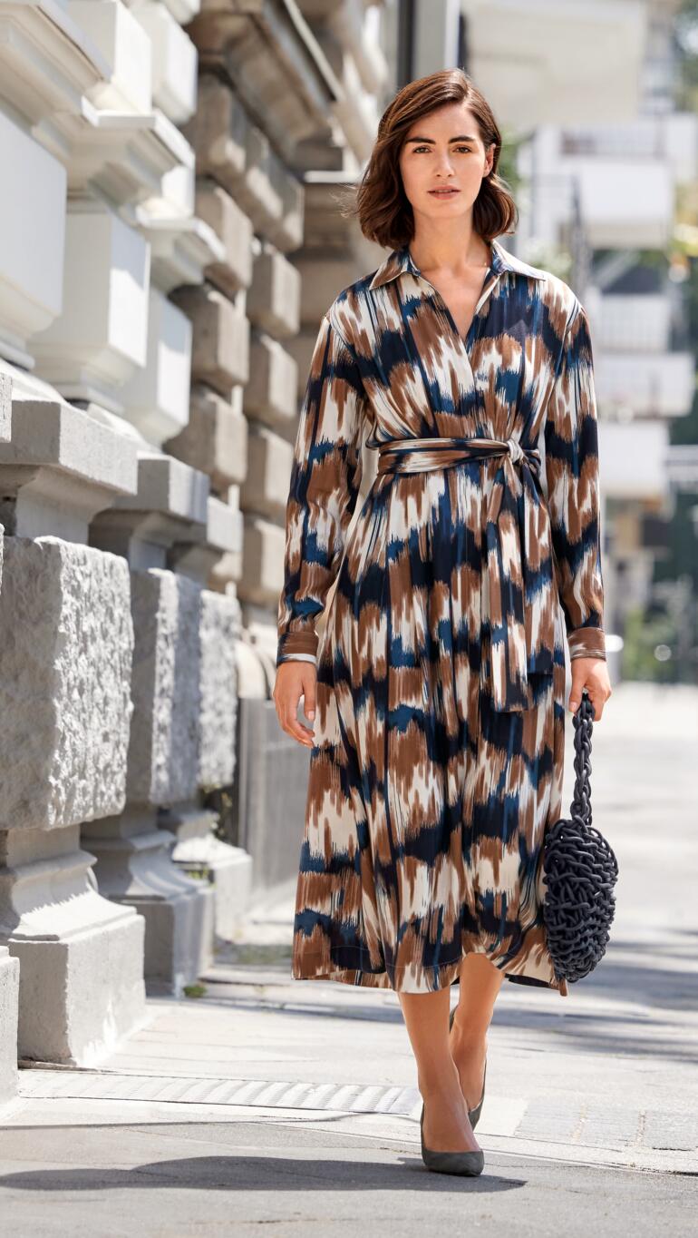 Figurschmeichelndes Everyday-Kleid Dame in figurschmeichelndem Kleid mit buntem Muster und Riemen auf der Straße.
