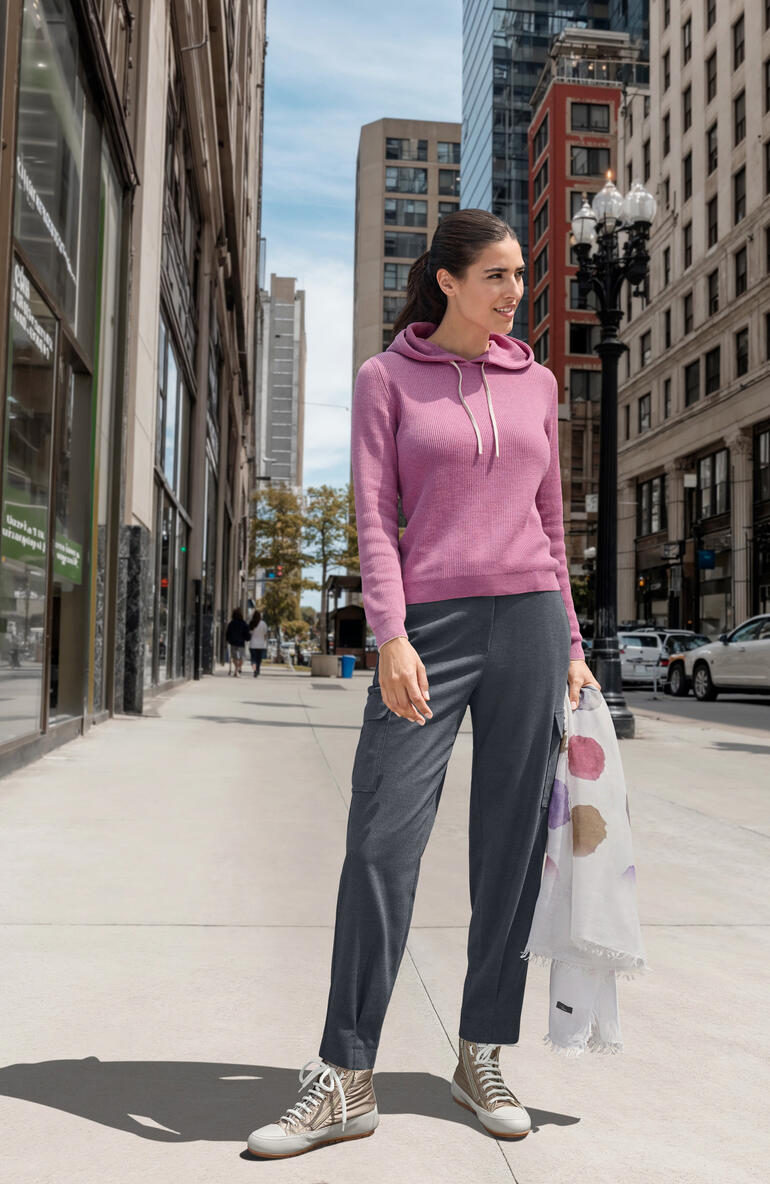 Candice Cooper Glam-Sneaker Frau im rosafarbenen Hoodie steht auf einer Stadtstraße.