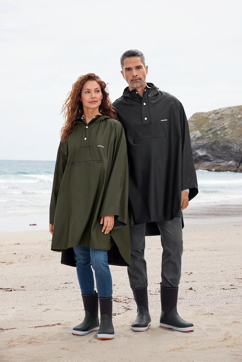 Oliv und Schwarz Regencape für Unisex von Tretorn, getragen von einem Mann und einer Frau am Strand.