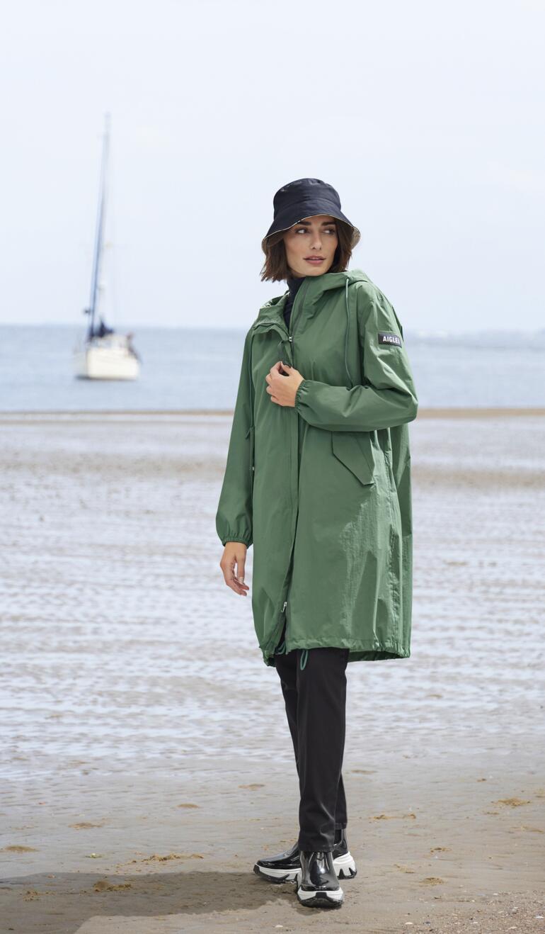 Frau in grünem Regenjacke und Chelsea-Sneakerboots am Strand.
