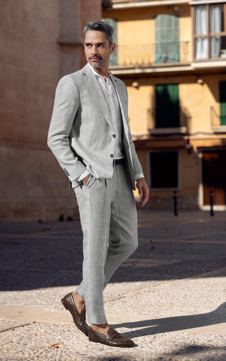 Mann in hellem Leinen-Anzug steht an einer Stadtstraße