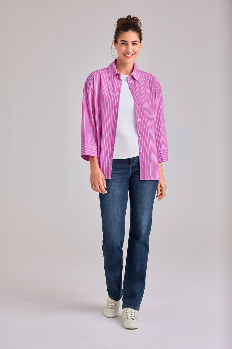 Frau in rosa Streifenbluse und Jeans steht lächelnd.