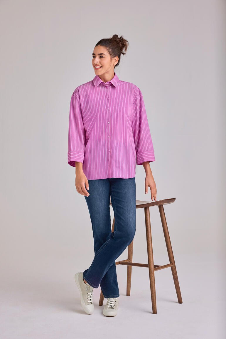 Rosa Streifenbluse 2.0, locker geschnitten, Modell steht an einem Hocker.