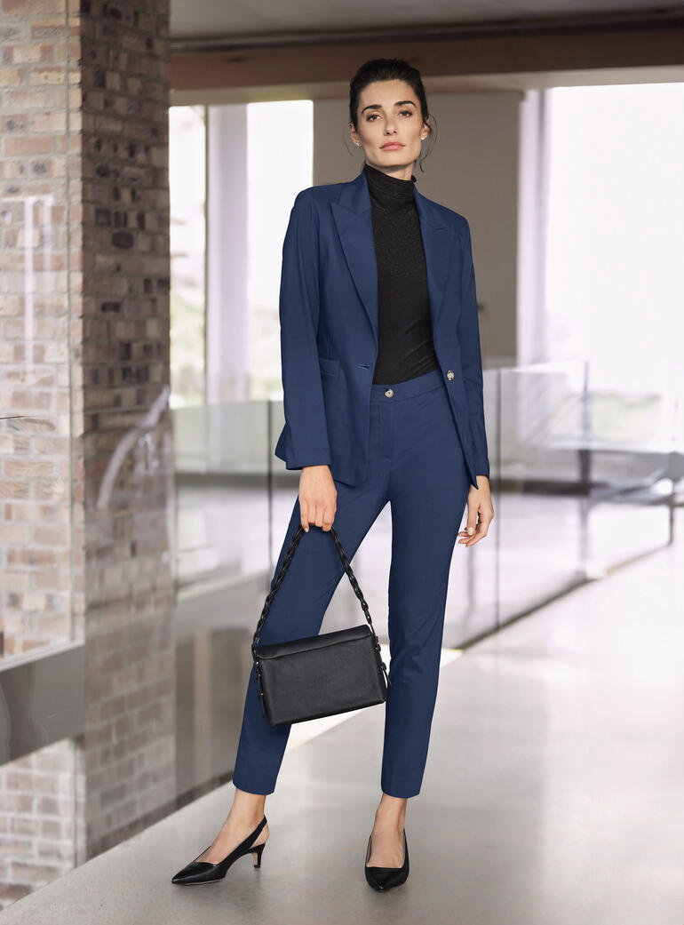 Frau in einem blauen Stretch-Anzug mit einer schwarzen Tasche.