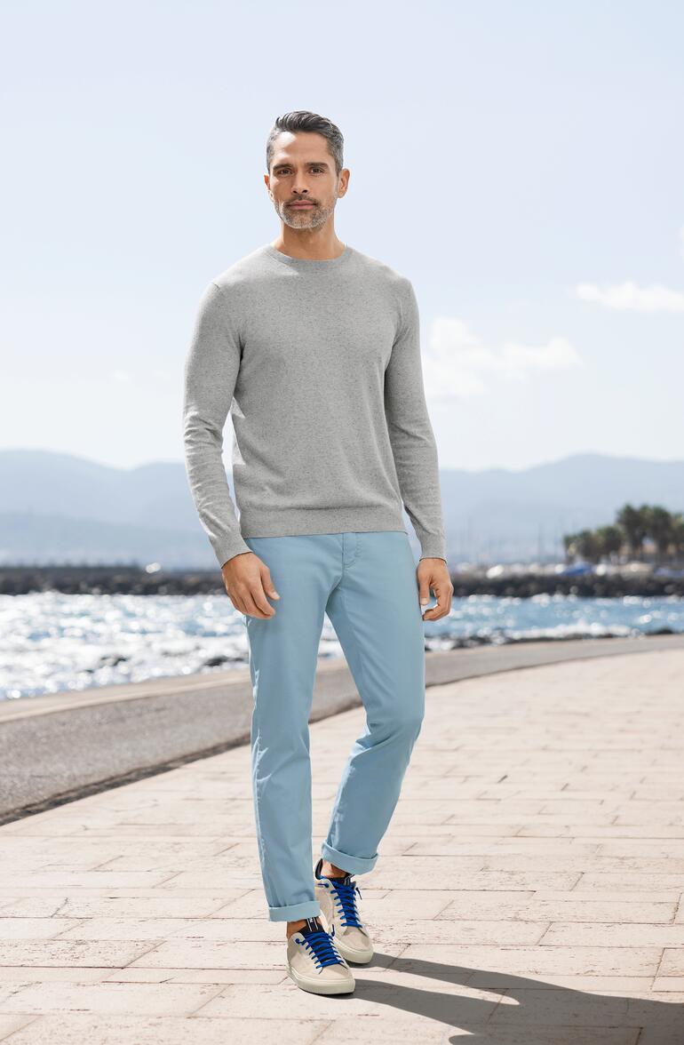 Mann in grauem Sommer-Tweed-Pullover und blauen Hosen am Strand.