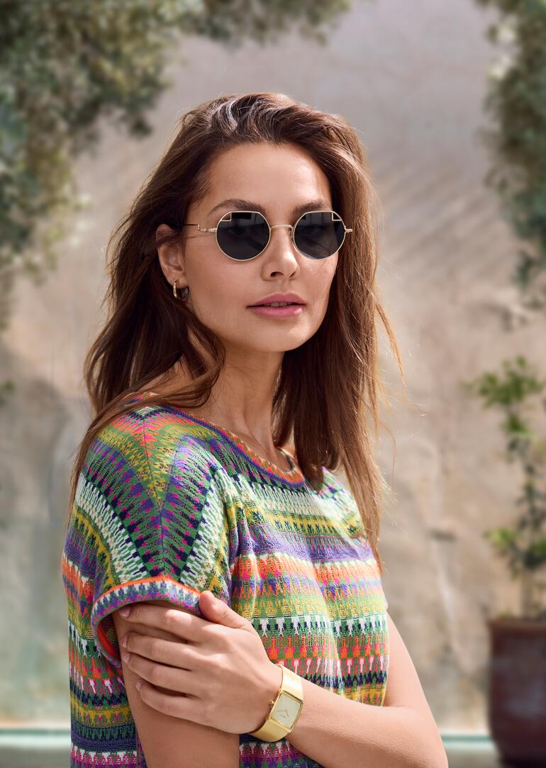 John Lennon Damen-Sonnenbrille Frau trägt runde John Lennon Damen-Sonnenbrille und ein buntes Oberteil