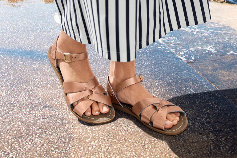 Füße in Salt-Water Ledersandalen auf einem nassen Boden.