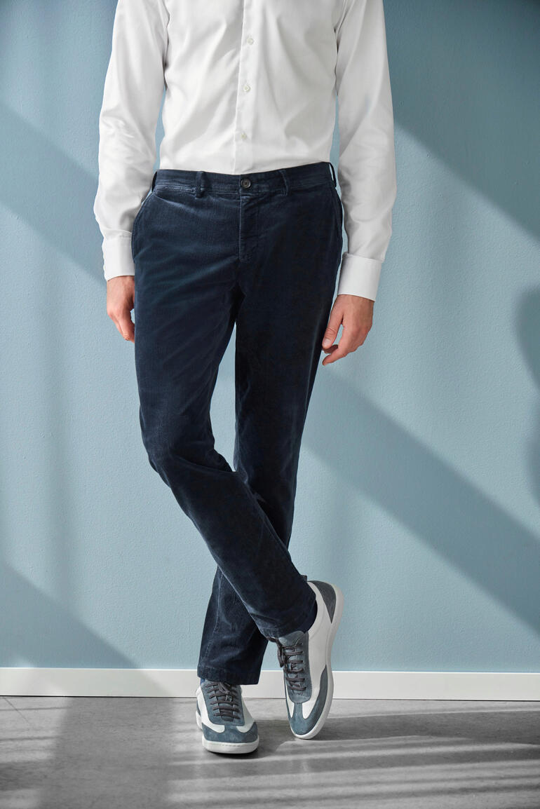 Mann trägt schwarze Samt-Hose, seitliche Ansicht vor einem blauen Hintergrund.