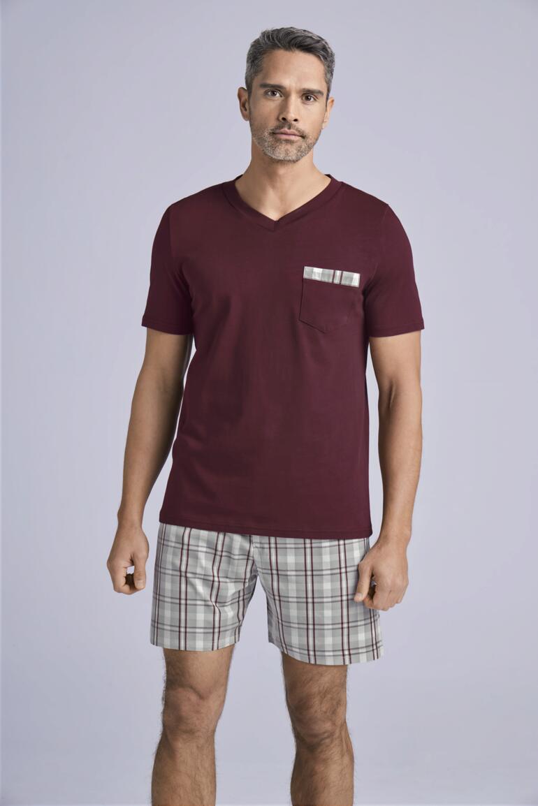 Mann in burgunderfarbenem T-Shirt mit kariertem Hut, trägt karierte Shorts.