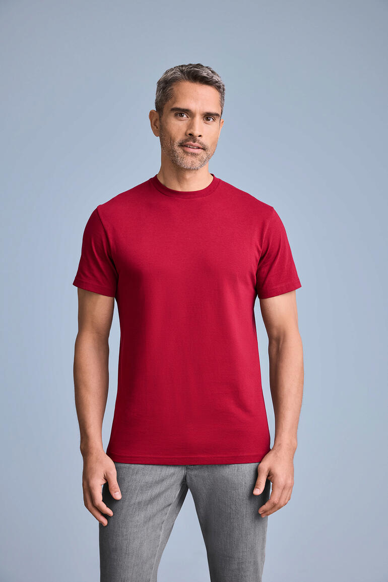 Mann trägt rotes T-Shirt mit Rundhalsausschnitt, poses vor grauem Hintergrund.