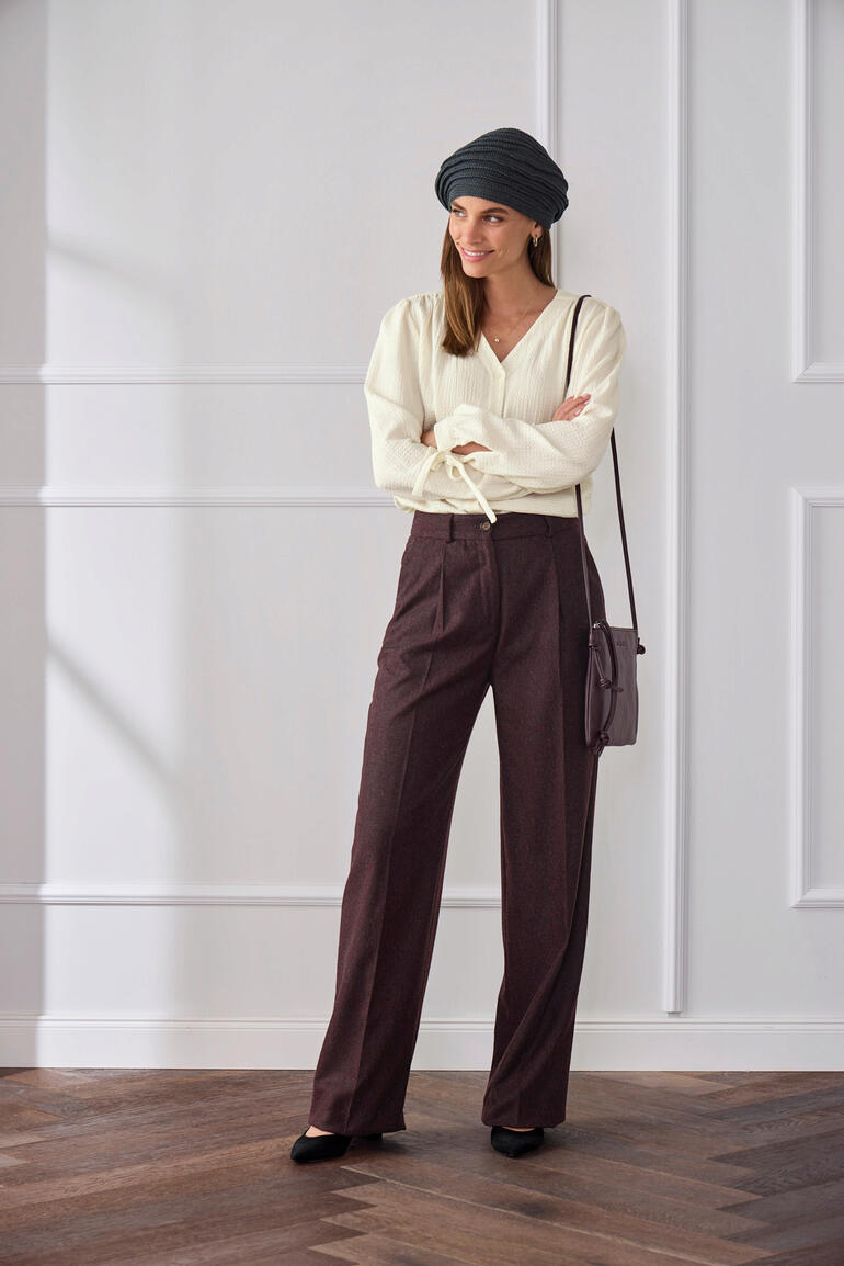 Frau in heller Baumwoll-Kaschmir-Bluse und braunen Hosen, mit Kopftuch.