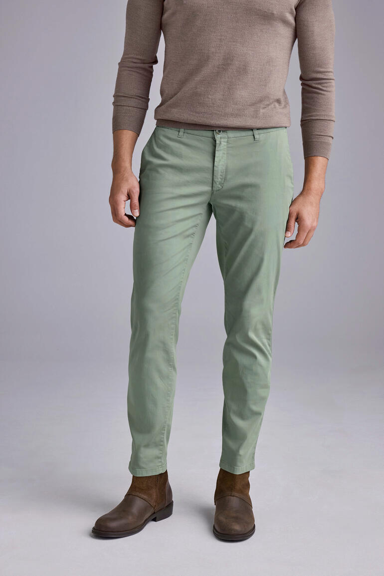 Mann in hellgrünen Chinos mit braunen Schuhen steht auf grauem Hintergrund.