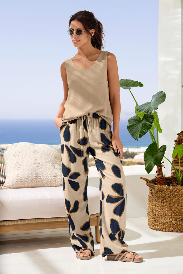 Frau in Urban Casual Loungewear mit beigen Oberteil und gemusterten Hosen auf einer Terrasse