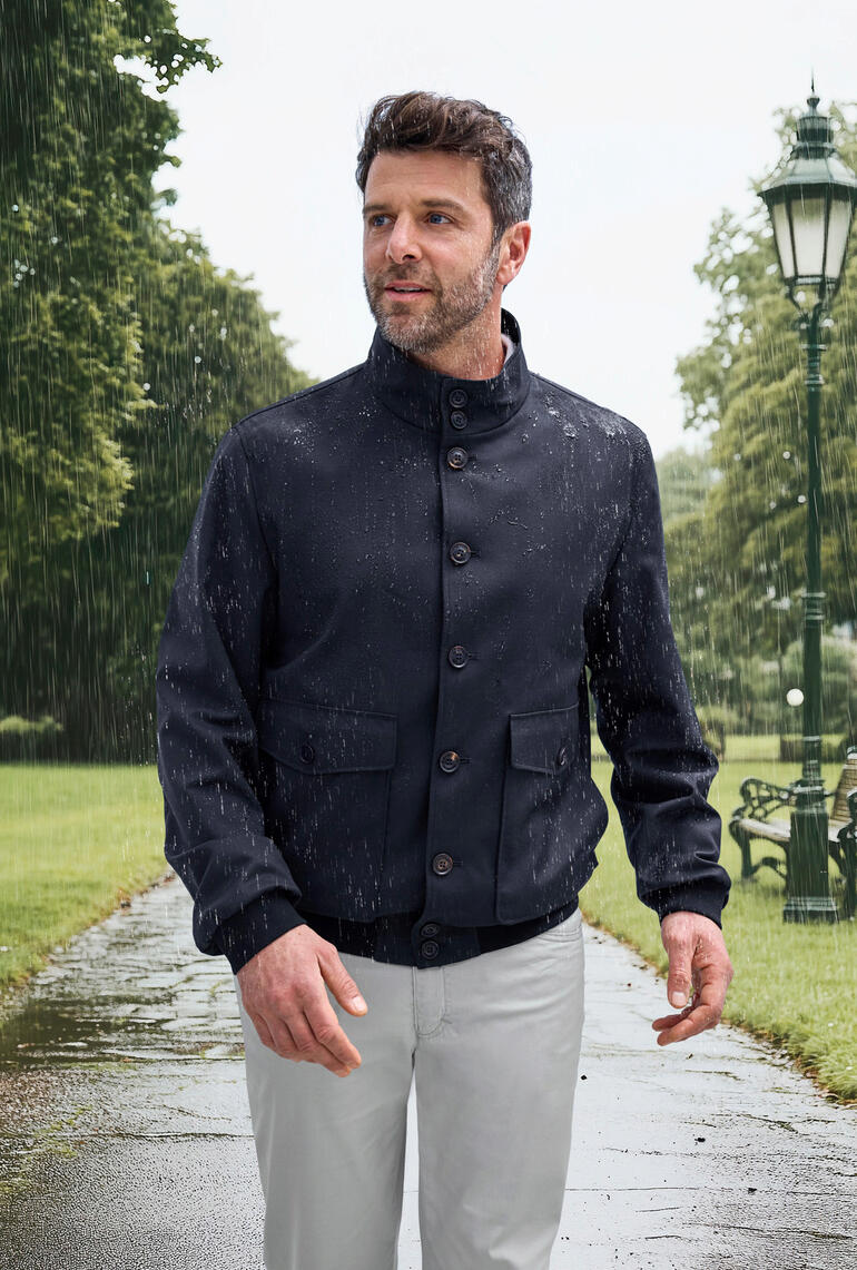Nähe eines Mannes im Storm-System®-Blouson, der Regen abfängt, blauer Hintergrund.