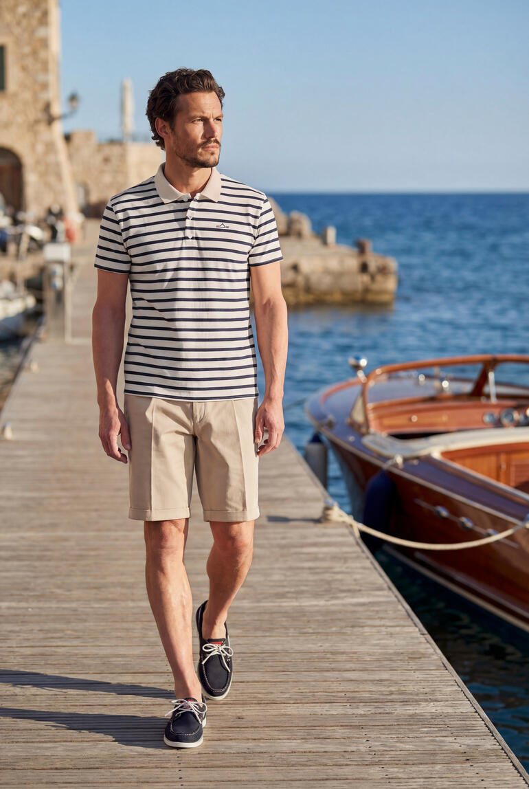 Mann trägt gestreiftes Poloshirt und Shorts am Hafen.