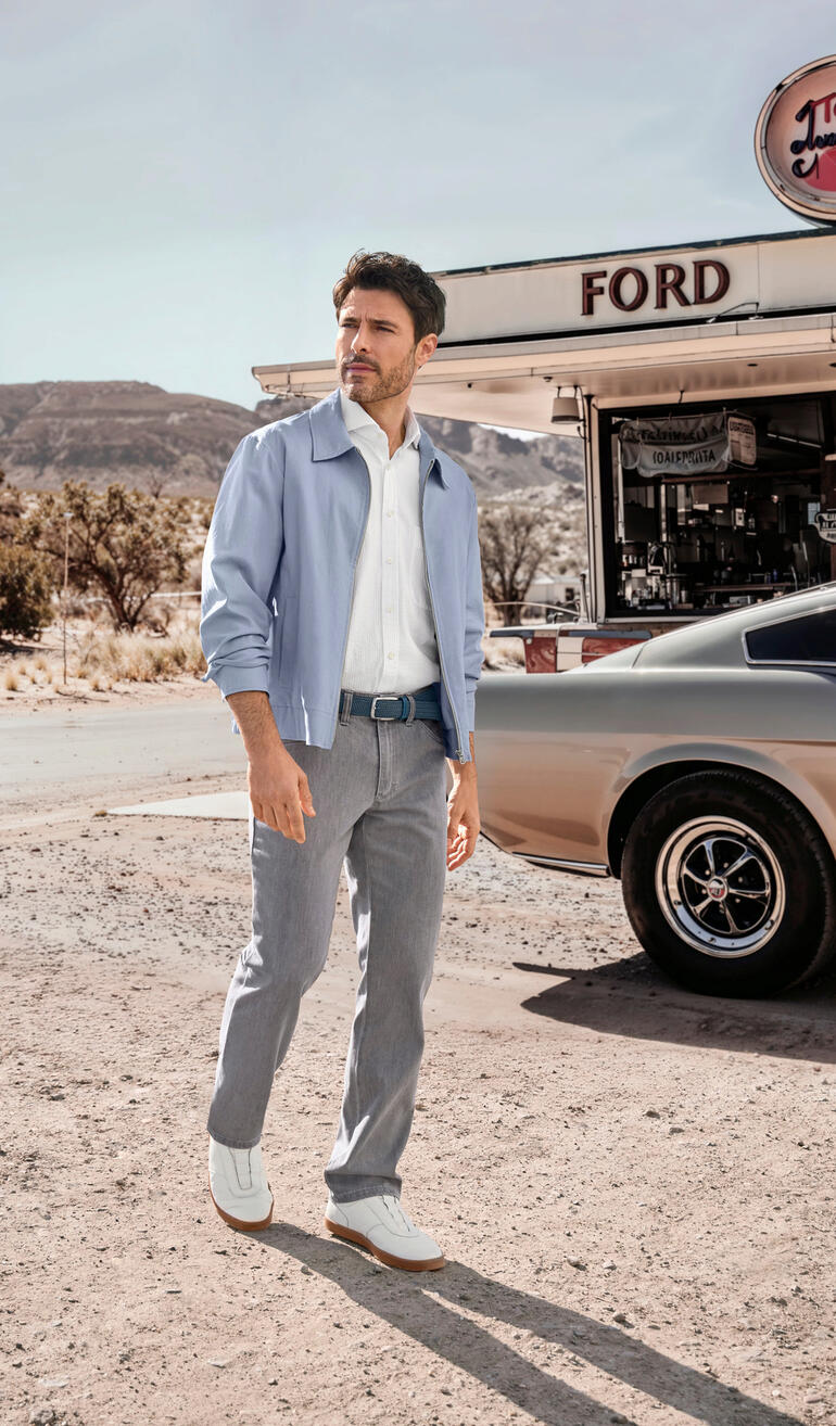 Leinen-Lyocell-Sommerblouson Mann in hellblauem Sommerblouson, steht vor einem Diner.
