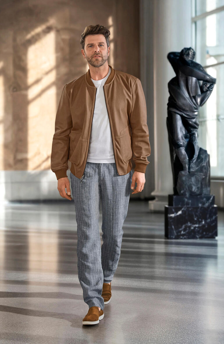 OCONI Metis-Wendeblouson Mann trägt einen braunen OCONI Metis-Wendeblouson, mit Statue im Hintergrund.