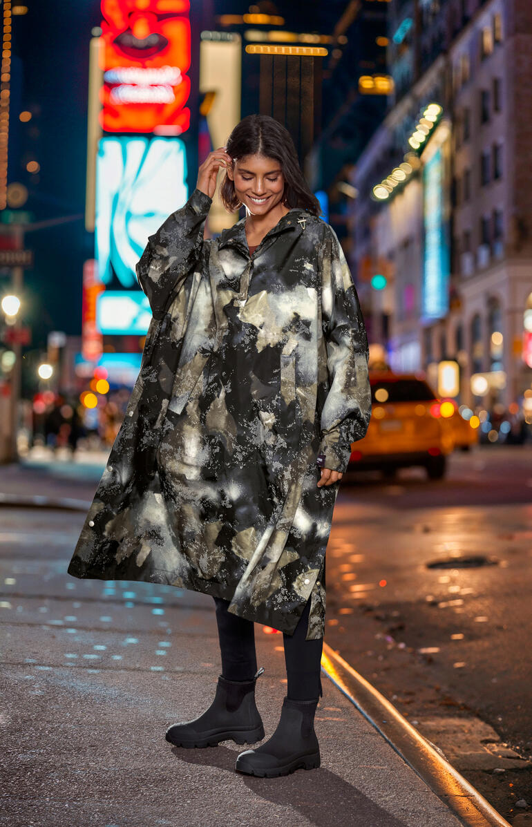 Ilse Jacobsen Design-Regenponcho Frau trägt ein gemustertes Regenponcho in einer Stadt bei Nacht.
