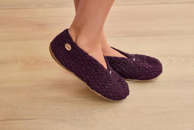 Kirgisische Hausschuhe in Berryfarbe stehen auf Holzfußboden