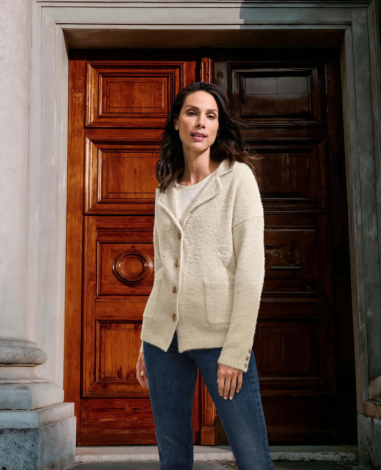 Frau in ecrufarbenem Strickblazer steht vor einer historischen Tür.