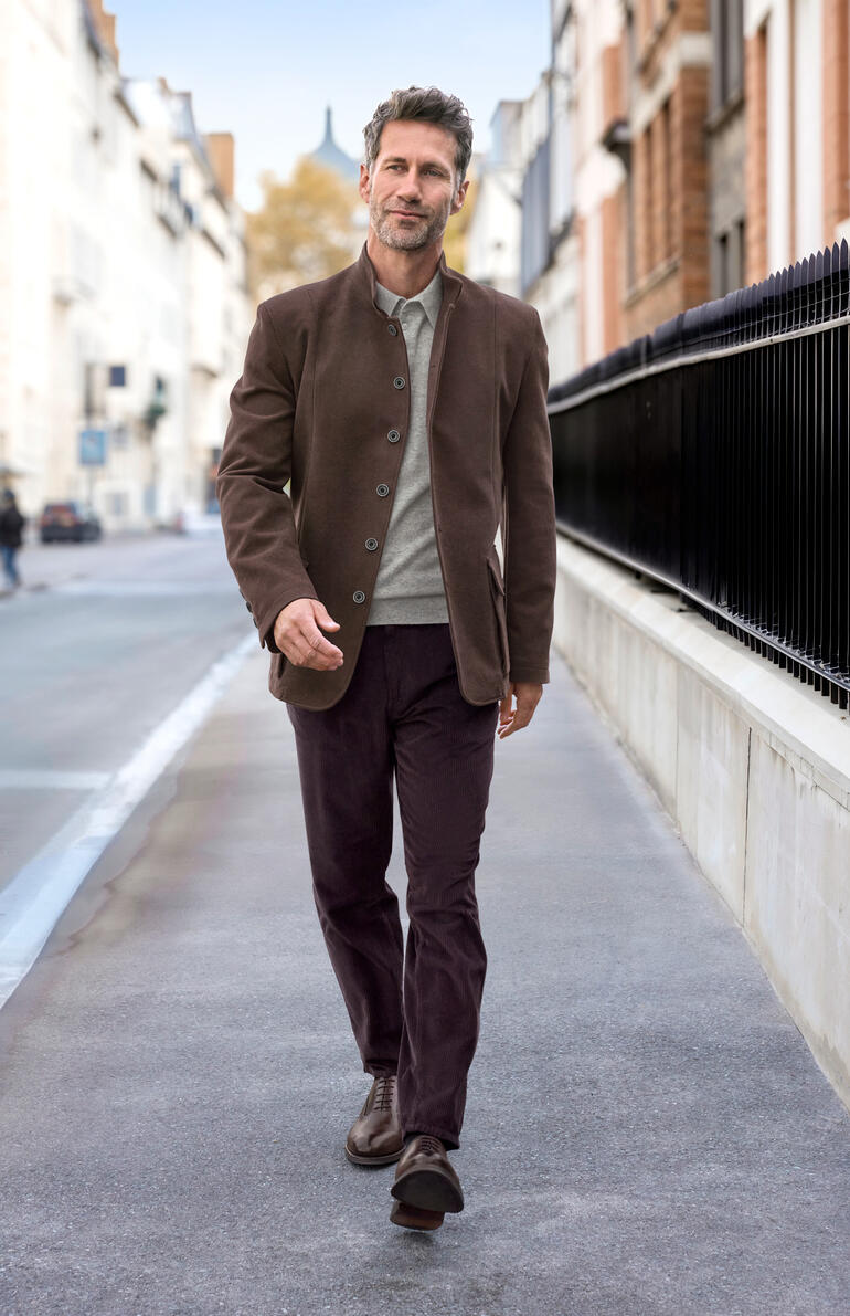 Mann in einem braunen Moleskin-Jacket geht in einer urbanen Umgebung